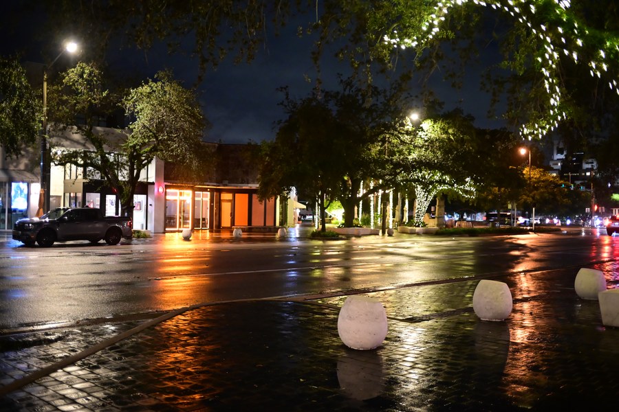 Wet paving and bollards facing the lighted storefronts